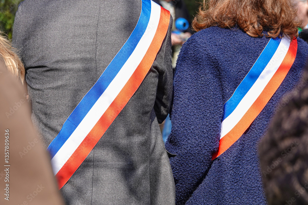 officials French elected avec tricolor sashes, backs turned, on ceremony outdoors during a sunny day in a public setting