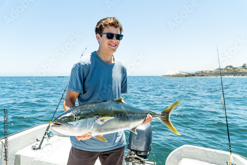 Obraz na płótnie A young brunette with glasses smiles proudly while holding a large fish freshly caught from the water, posing for a photo. w salonie