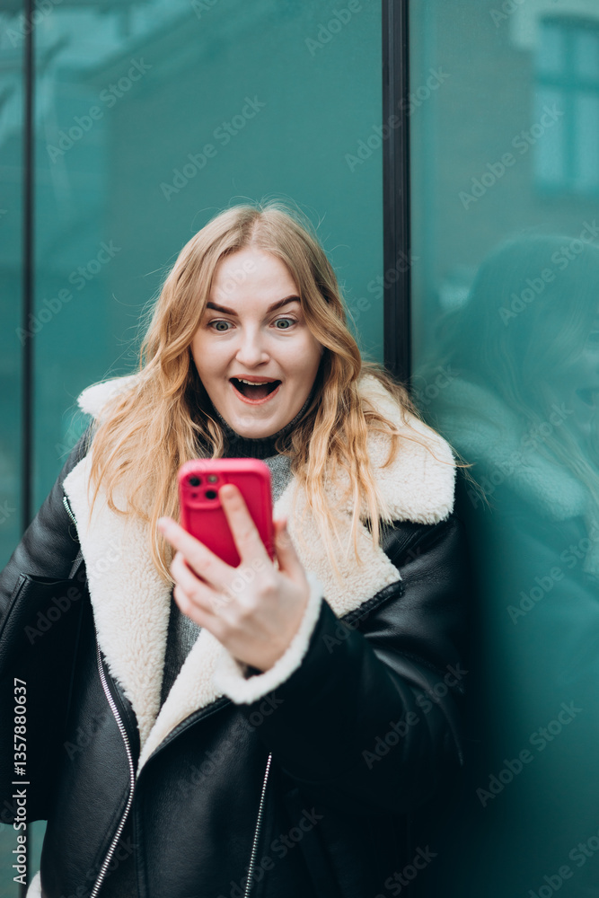 Smiling woman using mobile phone app, playing game, shopping online outdoors. Happy woman celebrating victory in lottery. Amazed hipster wondered with win in online auction betting on website