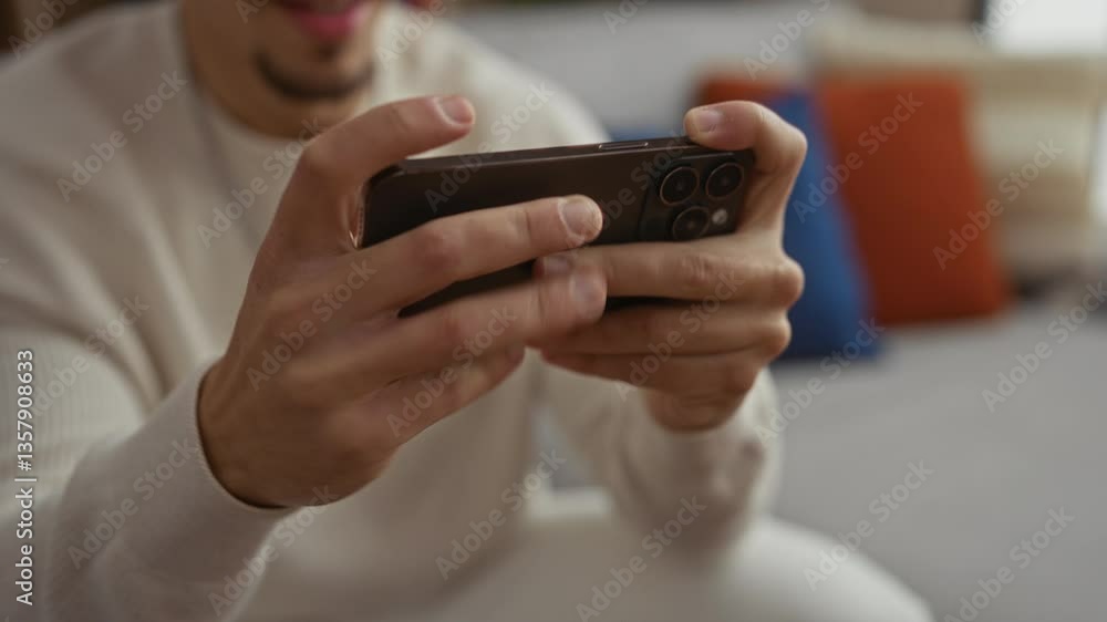 Young man in living room playing game on smartphone with focus and excitement, surrounded by cushions, wearing casual attire, engaged in indoor activity, showcasing modern technology. Young man in living room playing game on smartphone with focus and excitement, surrounded by cushions, wearing casual attire, engaged in indoor activity, showcasing modern technology.