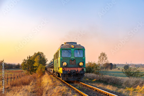 Powerful old diesel locomotive pulls a long freight train. Autumn sunset