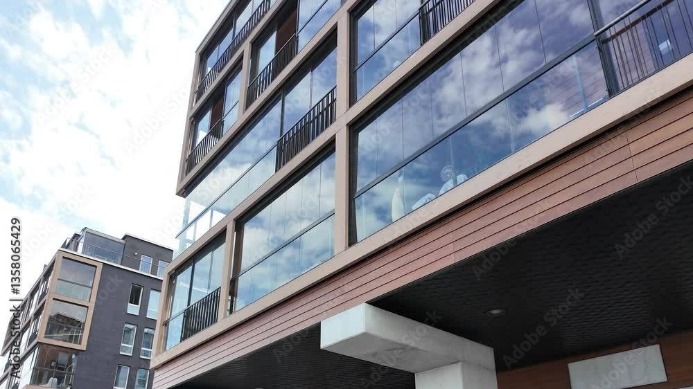 Modern residential building featuring expansive glass windows, wood paneling, and geometric structure, captured from a low angle under a partly cloudy sky. Modern residential building featuring expansive glass windows, wood paneling, and geometric structure, captured from a low angle under a partly cloudy sky.