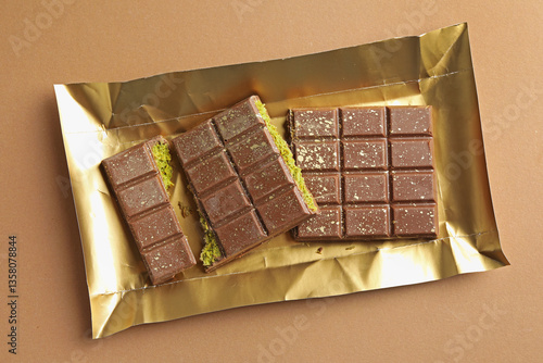 Photography Pieces of delicious Dubai chocolate with pistachios and knafeh on dark beige bac
