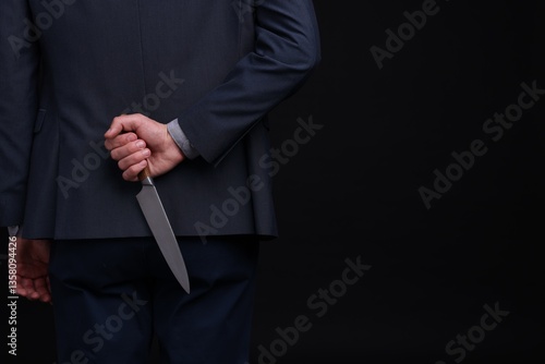 Foto Businessman holding knife behind his back on black background, closeup