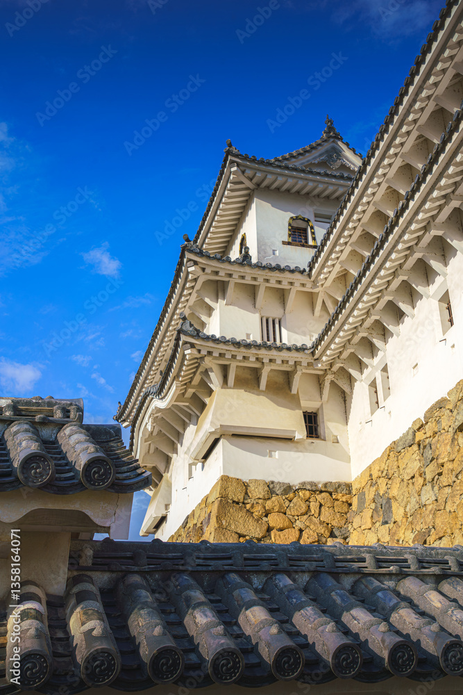 Obraz premium Himeji, Japan - Sep 24 2024, vertical, panoramic view of Himeji Castle, White Heron Castle from behind the roof of the castle outbuildings, in the daytime with blue sky, without people, Himeji, Japan