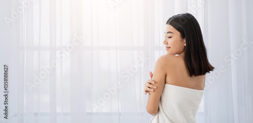 Free Download Joyful asian lady in towel touching her skin while standing by window at home. Young woman wrapped in white bath towel enjoying her soft skin after morning shower, panorama with copy space - GFXLoad