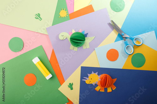 Fototapeta Naklejka Na Ścianę i Meble -  Colorful sheets of paper in various shades. Two playful 3D dinosaur crafts. DIY children craft and creative hobby for toy stores, art schools, and kindergartens