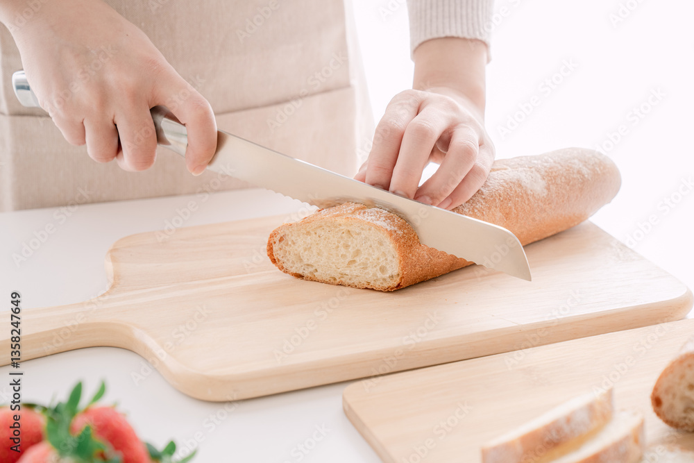 Close-up of hand slicing a crusty baguette with a serrated knife on a wooden cutting board Close-up of hand slicing a crusty baguette with a serrated knife on a wooden cutting board