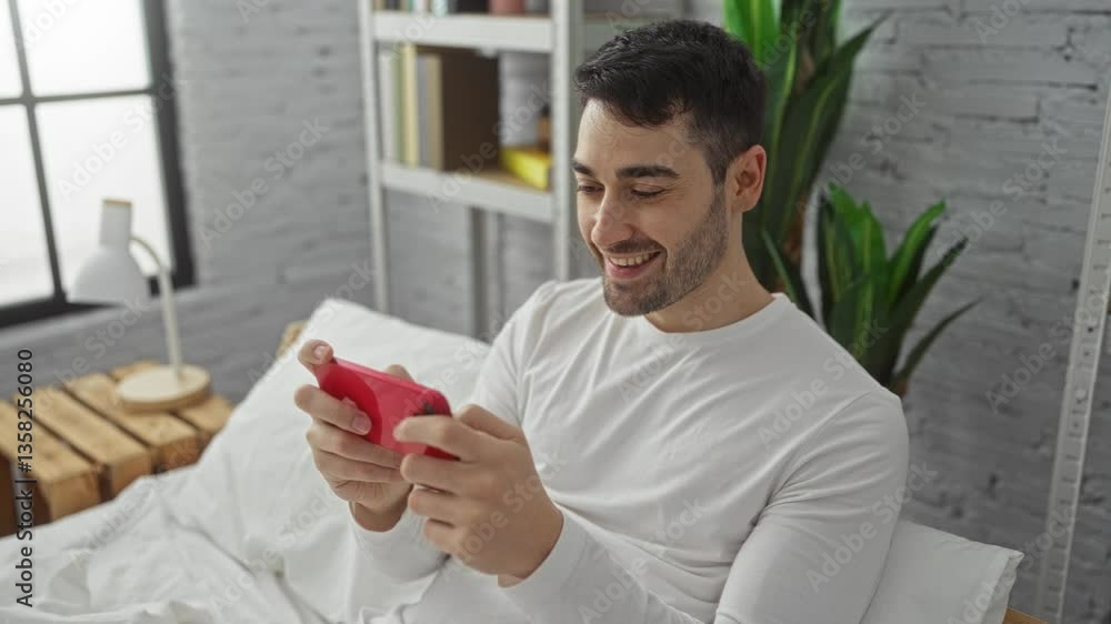 custom made wallpaper toronto digitalYoung man playing mobile game on bed in modern bedroom with a smile, surrounded by minimalist decor and houseplants, enjoying leisure time indoors.