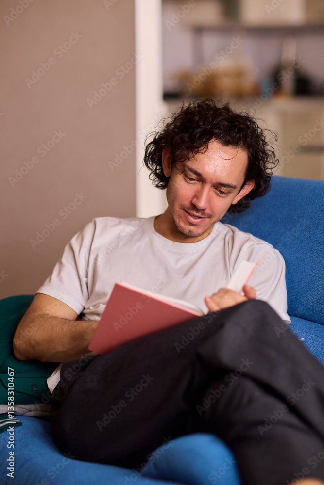 A Young Man Immersed in Reading a Book While Relaxing in a Cozy Living Room Atmosphere A Young Man Immersed in Reading a Book While Relaxing in a Cozy Living Room Atmosphere