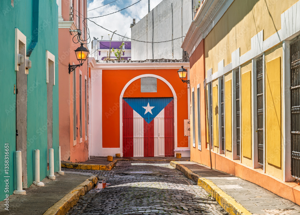 Fototapeta premium Charming cobblestone street in Old San Juan, Puerto Rico, with colorful colonial buildings featuring door painted with the Puerto Rican flag, vibrant scene full of culture and history (February 2025)