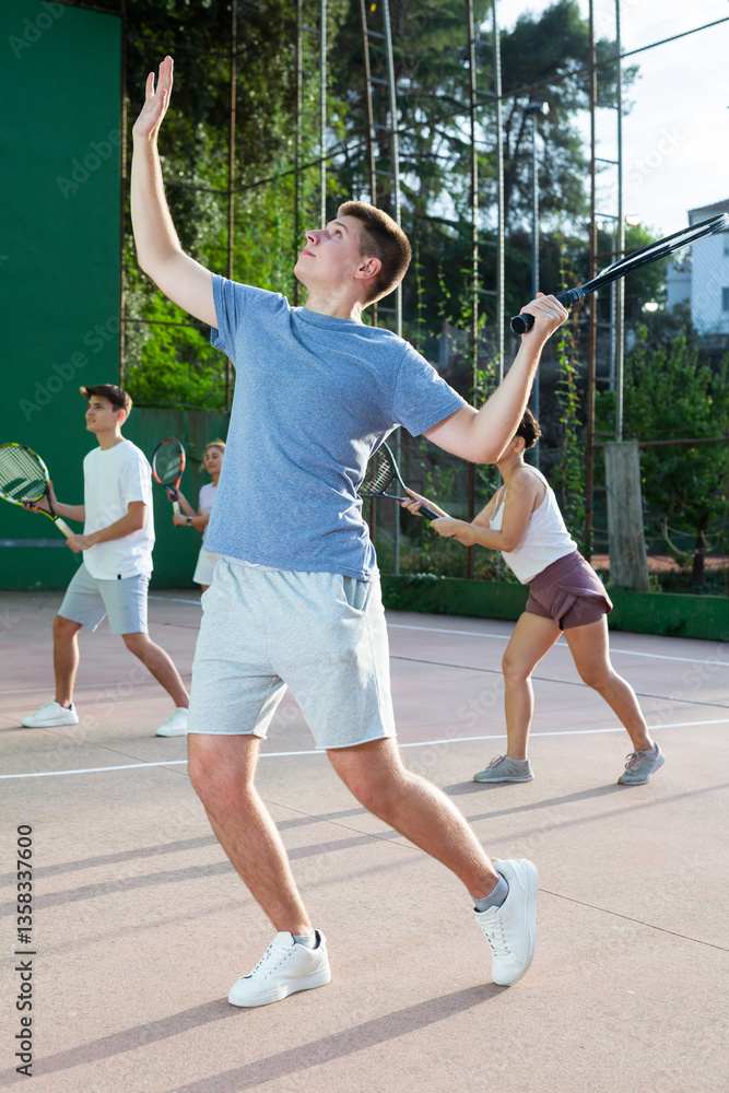 Fototapeta premium Positive motivated young frontenis player swinging string racquet to hit ball on outdoor walled court on sunny summer day. Sport and active lifestyle concept