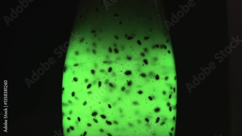 A bright green glowing liquid in a transparent bottle. Air bubbles rise up. Bubbles in the middle of plant seeds. The drink with plant seeds glows