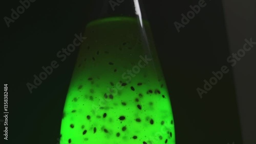 Top of the bottle. Liquid glowing with bright greenish light in a transparent bottle. On a dark black background, with a glare. Air bubbles rise up. Bubbles In the middle of the plant seeds. The drink