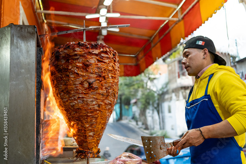 Street vendor slicing meat from a rotating trompo, or vertical spit, to prepare tacos al pastor at a street food stall