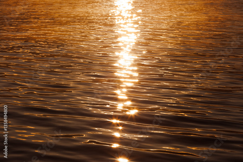 golden sunlight reflecting on gentle ripples of water during sunrise, creating a warm and shimmering path across the calm lake surface

