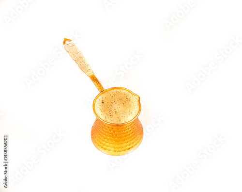 Turkish coffee pot (cezve) with foamy freshly brewed organic coffee isolated against a white background
