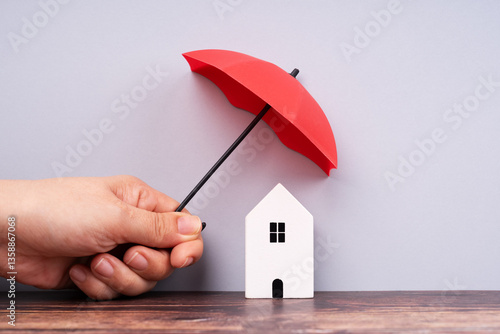 Family health and life insurance concept. White wooden mini house under a red umbrella.