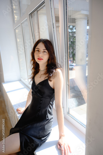 Free Download An elegant woman in black cloth sits on the windowsill, enjoying the warm sunshine. Young girl - GFXLoad