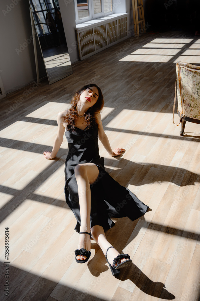 Obraz premium An elegant woman in black cloth is on the floor. enjoying the warm sleepy light. Young girl