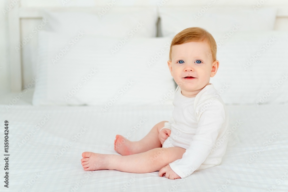 A cute little smiling baby boy in a white bodysuit is sitting on a bed at home in a bright bedroom, a six-month-old baby with blue eyes is smiling or laughing A cute little smiling baby boy in a white bodysuit is sitting on a bed at home in a bright bedroom, a six-month-old baby with blue eyes is smiling or laughing