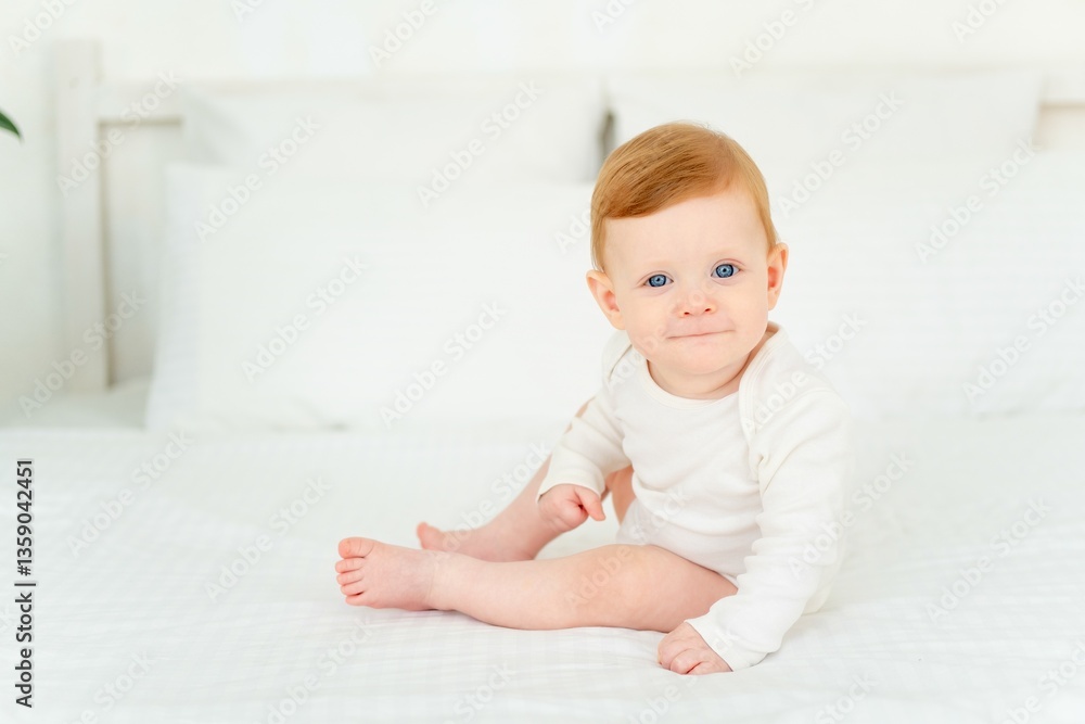 A cute little smiling baby boy in a white bodysuit is sitting on a bed at home in a bright bedroom, a six-month-old baby with blue eyes is smiling or laughing A cute little smiling baby boy in a white bodysuit is sitting on a bed at home in a bright bedroom, a six-month-old baby with blue eyes is smiling or laughing