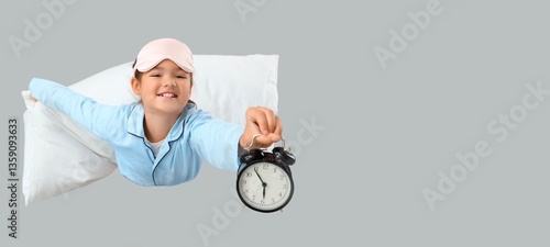 Happy little girl in pajamas, with blanket and alarm clock flying on grey bac...