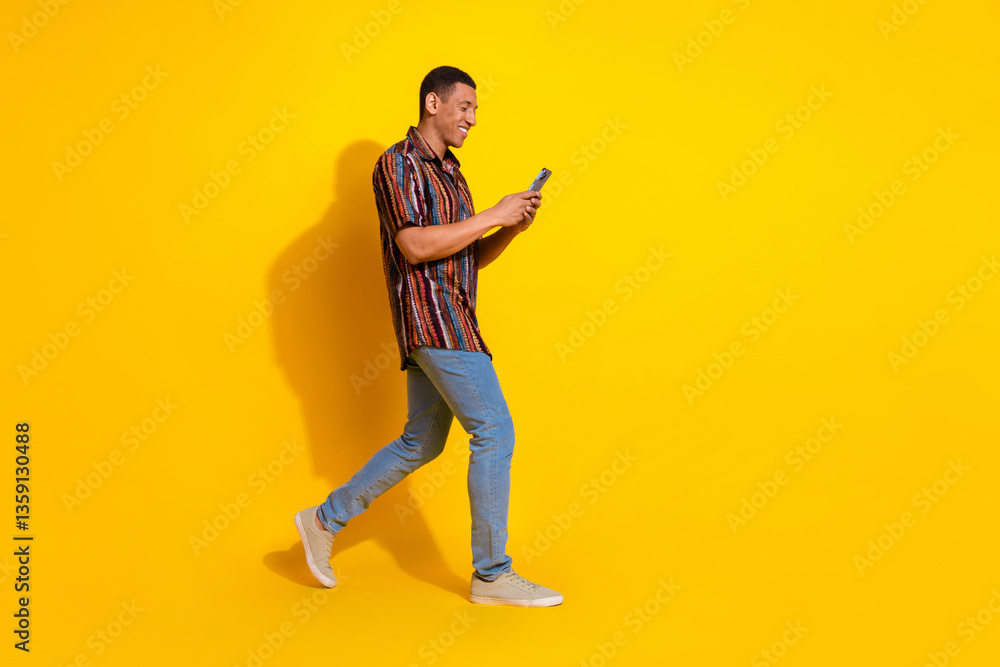 Young stylish man walking with phone against a bright yellow background expressing happiness and leisure Young stylish man walking with phone against a bright yellow background expressing happiness and leisure