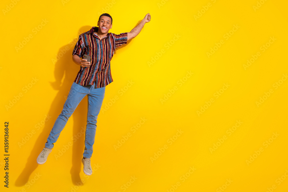 Young happy man holding a phone while jumping on a vibrant yellow background showcasing energy and positivity Young happy man holding a phone while jumping on a vibrant yellow background showcasing energy and positivity