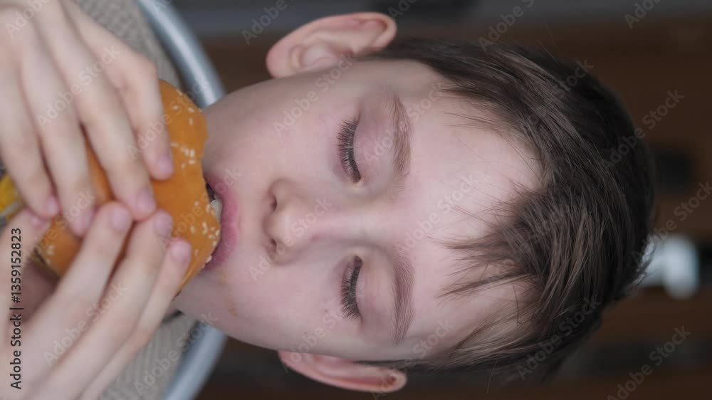 portrait of a Caucasian handsome boy 11 years old with pleasure eating an appetizing burger while inside, the child eats fast food with pleasure, vertical video portrait of a Caucasian handsome boy 11 years old with pleasure eating an appetizing burger while inside, the child eats fast food with pleasure, vertical video