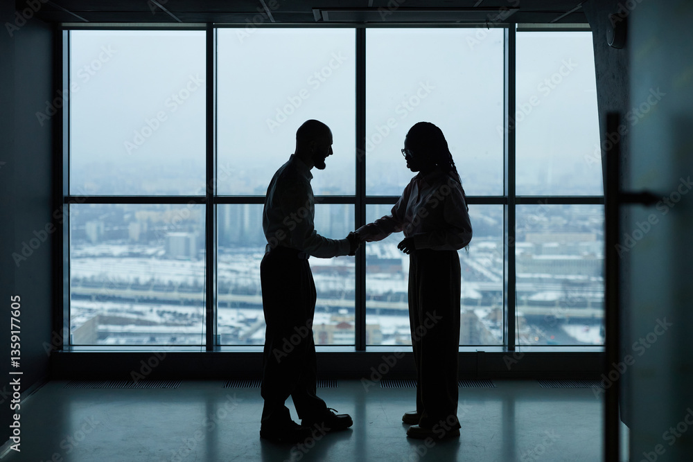 Fototapeta premium Colleagues shaking hands to each other while standing against panoramic window in office hall