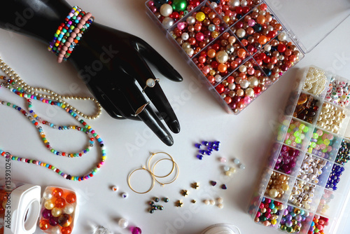 Hand figurine, colorful friendship bracelets, necklaces, various beads and DIY supplies on the table. Making jewelry at home. Flat lay.