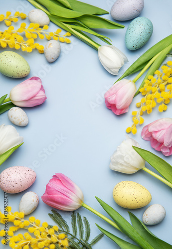 Easter eggs and tulips forming a frame on light blue background