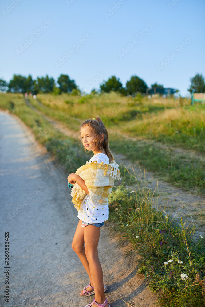 Young girl in summer attire with a yellow shawl enjoying a sunny day in a grassy field near a winding path Young girl in summer attire with a yellow shawl enjoying a sunny day in a grassy field near a winding path