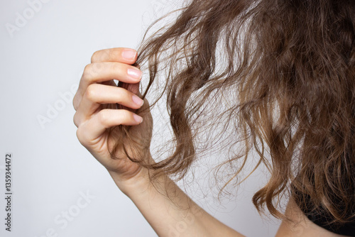 Woman holding tangled dry hair in hand. Isolated on grey background. Curly and frizzy hair problems, damage, hair loss, brittleness, split ends. Beauty and health concept
