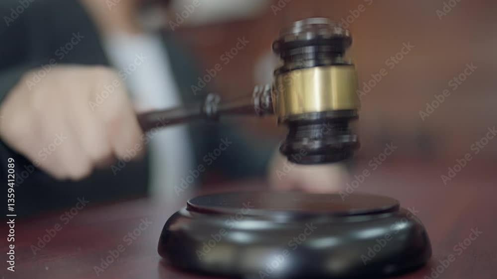 A judge is holding a gavel and sitting at a desk. The gavel is on a wooden surface A judge is holding a gavel and sitting at a desk. The gavel is on a wooden surface