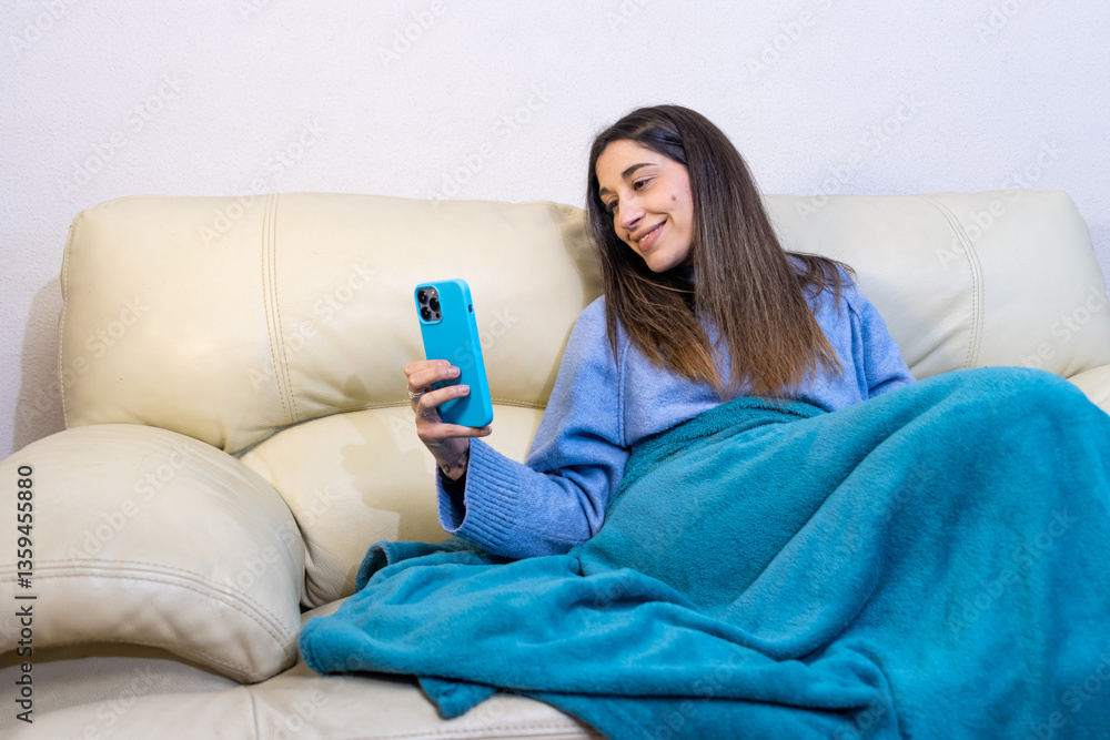 Young woman relaxing on sofa using smartphone at night Young woman relaxing on sofa using smartphone at night