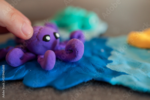 Children playing with colorful sea animals made from modeling clay, including a purple octopus, green fish, yellow starfish, and a red volcano on a blue ocean base photo