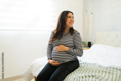 Free Download Expectant mother resting on bed, gently touching growing bump with warm smile, radiating maternal love and pregnancy happiness - GFXLoad