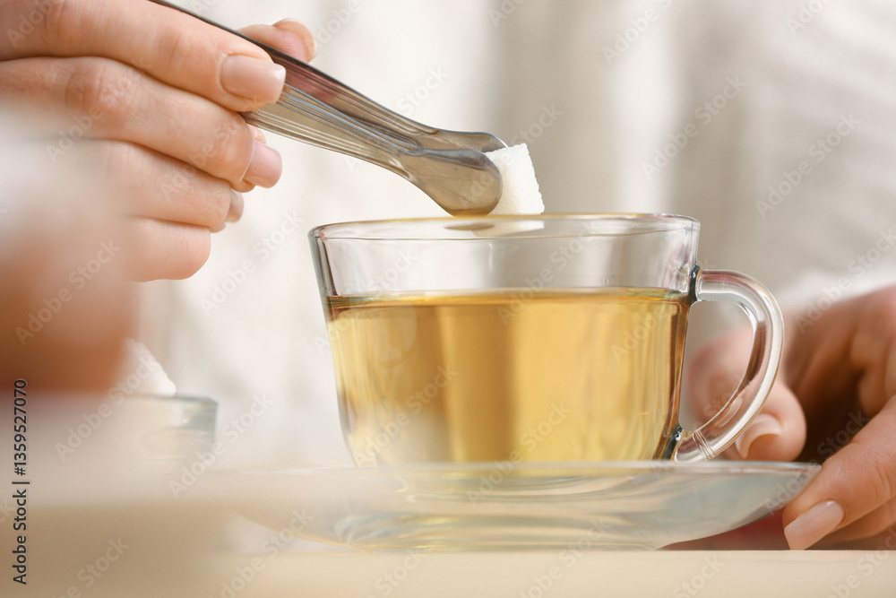 Woman putting lump of sugar into tea at table in kitchen. Closeup Woman putting lump of sugar into tea at table in kitchen. Closeup