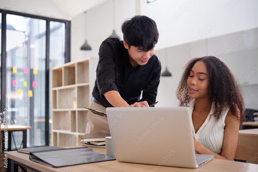 Two diverse professionals engage in a discussion while working on a laptop. Two diverse professionals engage in a discussion while working on a laptop.