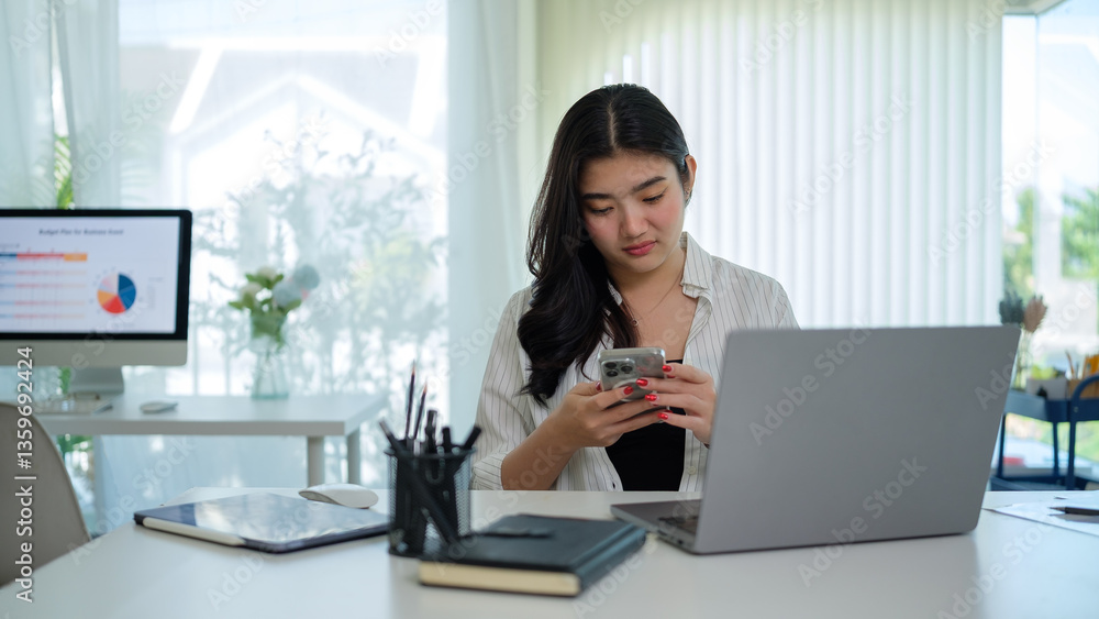Young entrepreneur sitting in modern office with laptop and checking her mobile phone. Young entrepreneur sitting in modern office with laptop and checking her mobile phone.