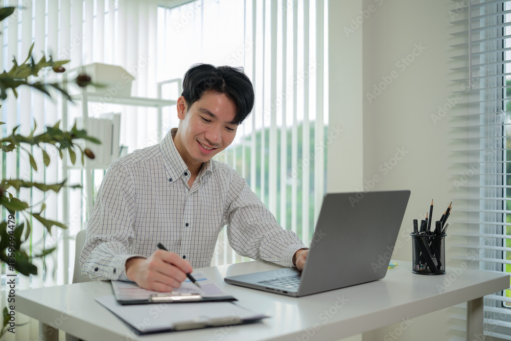 Fototapeta premium Smiling man engaged in his work, balancing digital and handwritten notes in a beautifully designed home office.