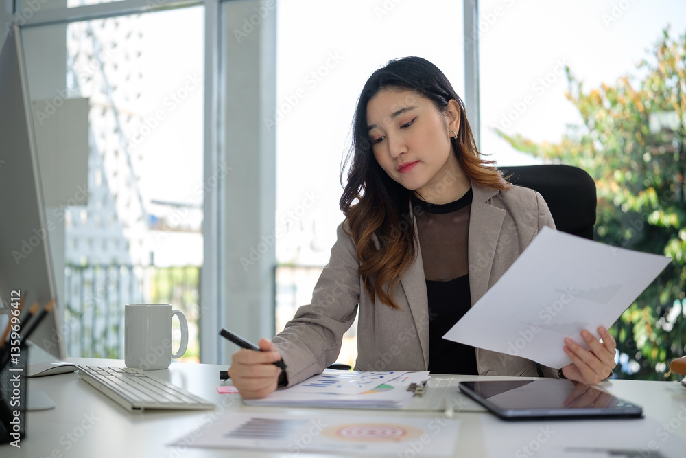 Young female entrepreneur concentrates on her work, analyzing data and writing notes while seated at a sleek, contemporary office desk. Young female entrepreneur concentrates on her work, analyzing data and writing notes while seated at a sleek, contemporary office desk.