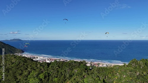 Paragliders soaring above coastline with clear skies at sunset