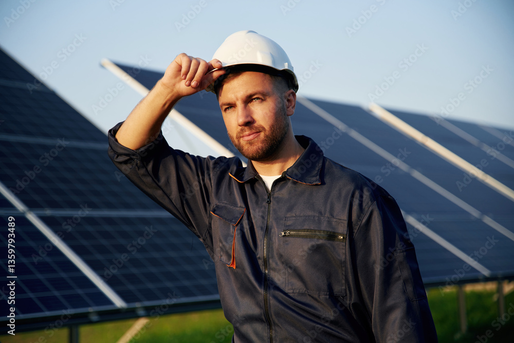Touching the white hard hat. Man is working with solar panels outdoors at daytime Touching the white hard hat. Man is working with solar panels outdoors at daytime