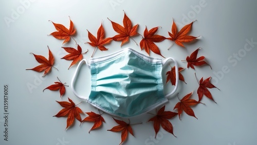 A medical mask surrounded by autumn leaves on a white background, serving as protection against colds during the cold season, with the virus aggravation depicted in a flat layout from a top view.