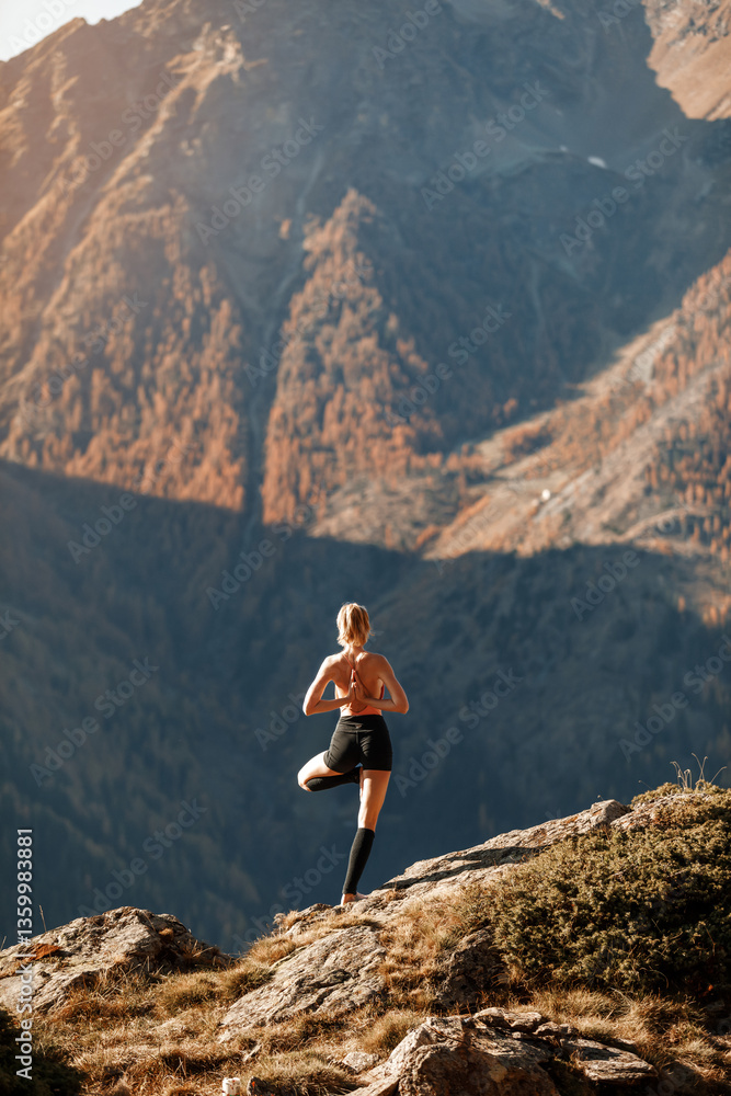 Fototapeta premium A young slender girl does yoga against the backdrop of beautiful nature among the mountains. Healthy lifestyle concept