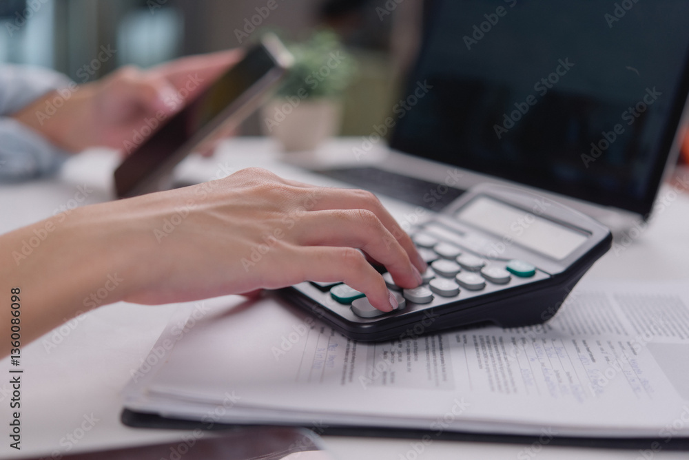 Office worker performing calculations with a calculator and smartphone on the table, analyzing business data or financial reports. Office worker performing calculations with a calculator and smartphone on the table, analyzing business data or financial reports.