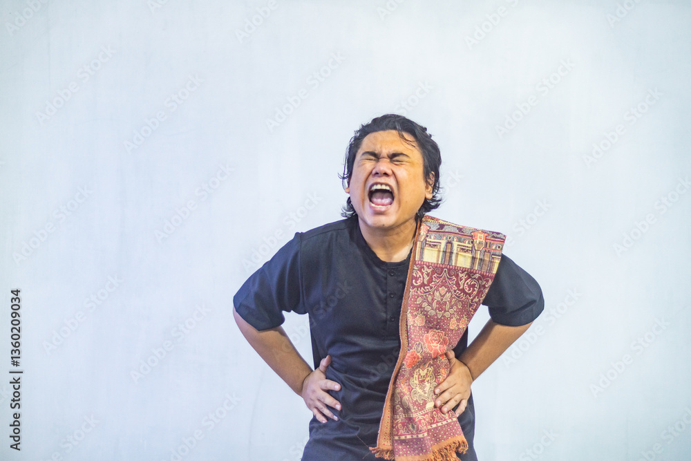 Portrait of young Asian Muslim man holding his stomach because of hunger while fasting. Ramadan and Eid concept.